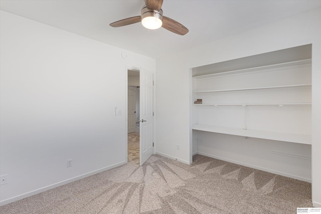 unfurnished bedroom with built in desk, light colored carpet, ceiling fan, and a closet