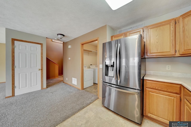 kitchen featuring independent washer and dryer, stainless steel fridge with ice dispenser, light carpet, light brown cabinets, and a textured ceiling