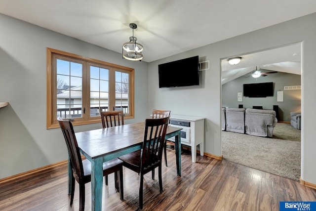 dining area featuring dark hardwood / wood-style flooring, ceiling fan with notable chandelier, and vaulted ceiling