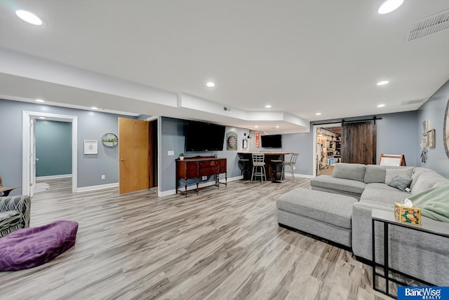 living room featuring light hardwood / wood-style flooring, a barn door, and bar area