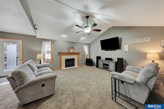 carpeted living room featuring a textured ceiling, vaulted ceiling, a tile fireplace, and ceiling fan