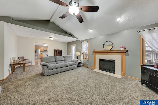 carpeted living room featuring a tiled fireplace, plenty of natural light, lofted ceiling with beams, and ceiling fan