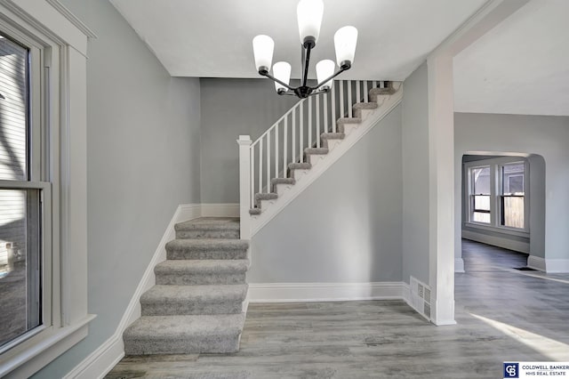 staircase with hardwood / wood-style floors and a chandelier