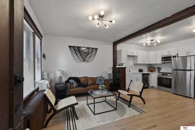 living room with beamed ceiling, sink, light hardwood / wood-style flooring, and a textured ceiling