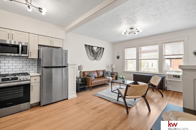 kitchen featuring appliances with stainless steel finishes, radiator, white cabinets, decorative backsplash, and light hardwood / wood-style flooring