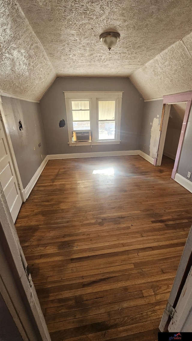 additional living space with cooling unit, dark hardwood / wood-style flooring, vaulted ceiling, and a textured ceiling