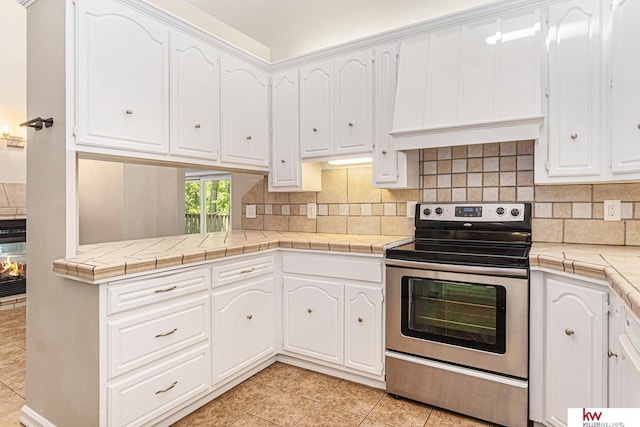 kitchen with stainless steel electric stove, tile countertops, and white cabinets