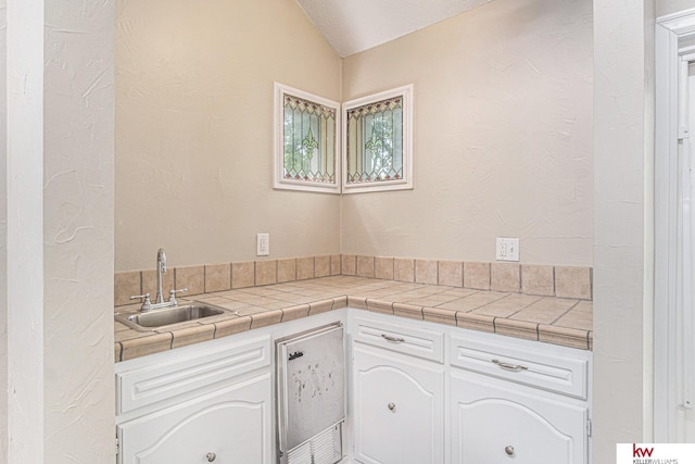 kitchen with vaulted ceiling, tile countertops, sink, and white cabinets