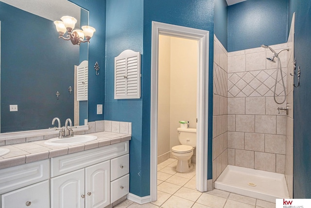 bathroom featuring a tile shower, tile patterned flooring, vanity, a notable chandelier, and toilet