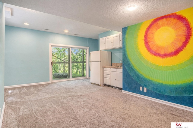 unfurnished bedroom featuring white fridge, sink, light colored carpet, and a textured ceiling