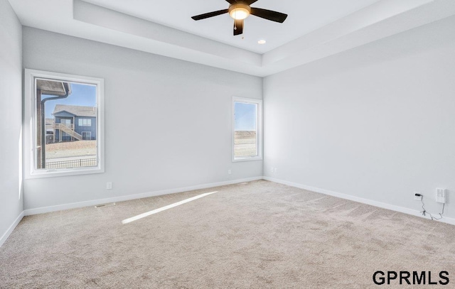 carpeted spare room with ceiling fan and a raised ceiling