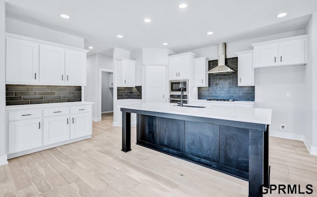 kitchen featuring built in microwave, sink, white cabinets, a center island with sink, and wall chimney exhaust hood