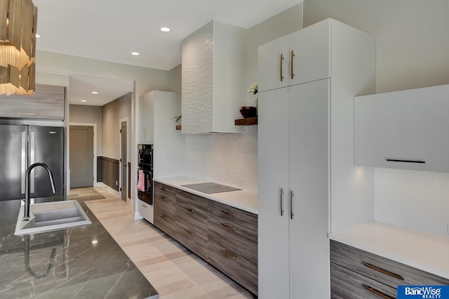 kitchen with sink, white cabinetry, black appliances, decorative backsplash, and light wood-type flooring