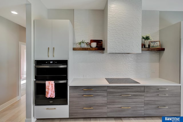 kitchen with multiple ovens, black electric stovetop, light hardwood / wood-style floors, and decorative backsplash