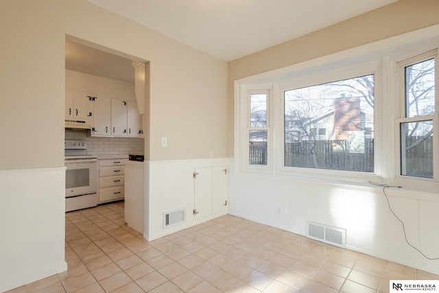 kitchen with tasteful backsplash, white cabinetry, white electric range, and light tile patterned floors