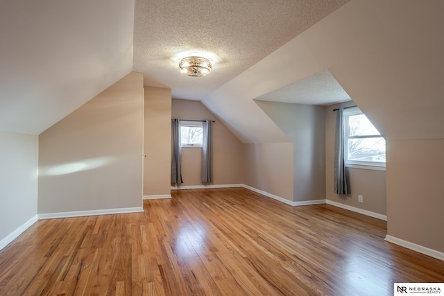 bonus room featuring vaulted ceiling, a wealth of natural light, a textured ceiling, and light hardwood / wood-style flooring