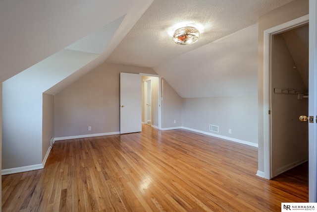 bonus room featuring light hardwood / wood-style flooring, a textured ceiling, and vaulted ceiling