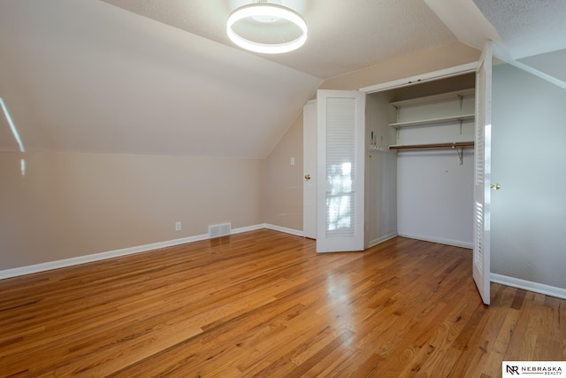 bonus room with vaulted ceiling, a textured ceiling, and light hardwood / wood-style flooring