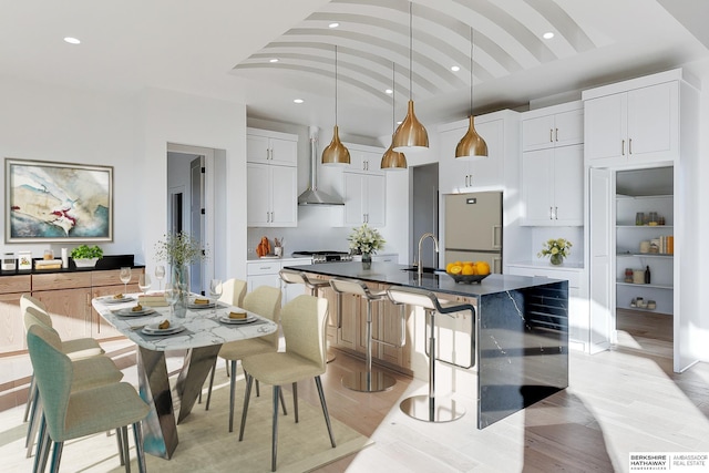 kitchen with decorative light fixtures, white cabinetry, an island with sink, fridge, and wall chimney exhaust hood