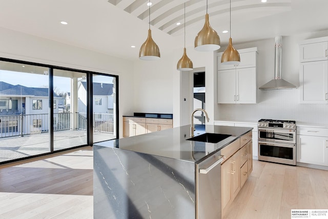 kitchen with appliances with stainless steel finishes, white cabinetry, an island with sink, sink, and wall chimney exhaust hood