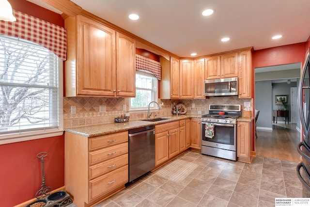 kitchen with appliances with stainless steel finishes, sink, backsplash, and light stone counters