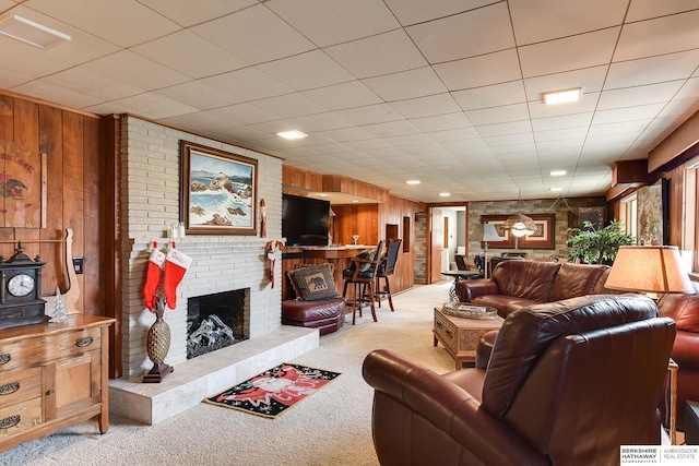 carpeted living room with a fireplace and wood walls