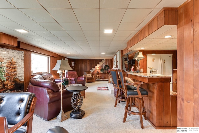 living room with light colored carpet, bar, and wood walls