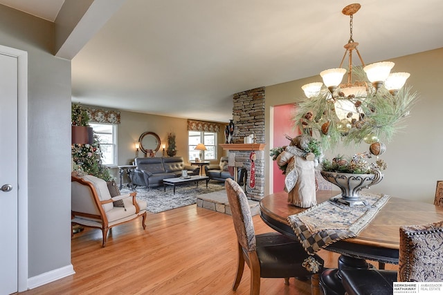 dining space with an inviting chandelier, a stone fireplace, and light hardwood / wood-style flooring