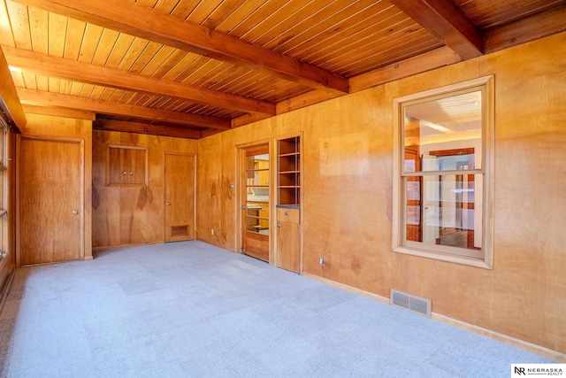 spare room featuring wooden walls, wooden ceiling, built in shelves, light colored carpet, and beamed ceiling