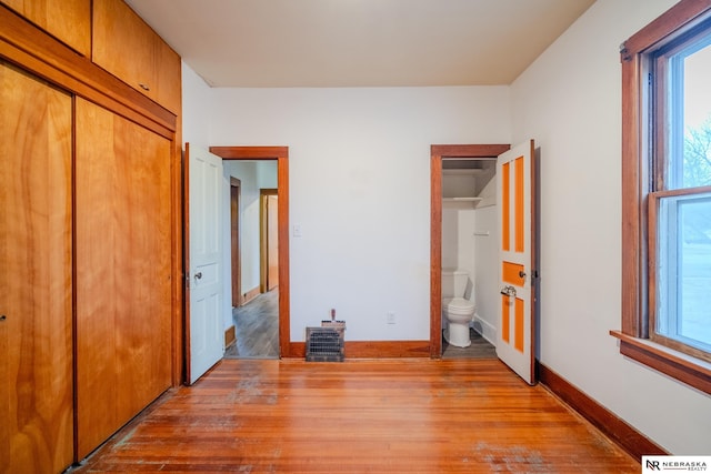 unfurnished bedroom featuring multiple windows, connected bathroom, light hardwood / wood-style flooring, and a closet