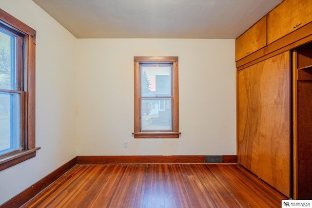 unfurnished bedroom with multiple windows, dark hardwood / wood-style floors, and a closet