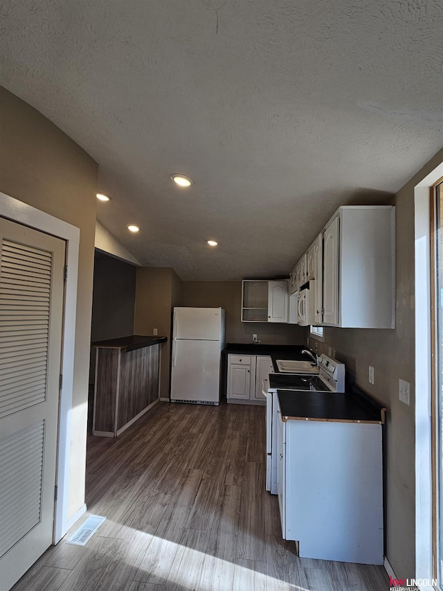 kitchen with white appliances, dark wood-type flooring, a textured ceiling, and white cabinets