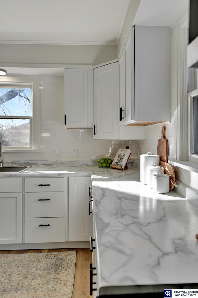 kitchen with sink, white cabinetry, light stone counters, light hardwood / wood-style flooring, and decorative backsplash