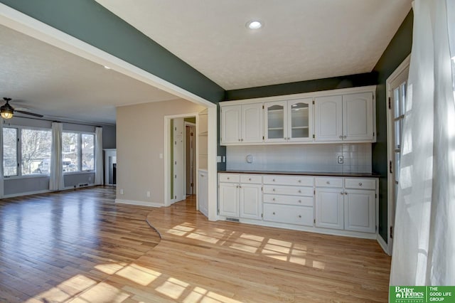 kitchen featuring white cabinetry, decorative backsplash, ceiling fan, and light hardwood / wood-style flooring