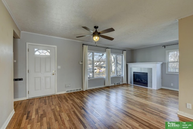 unfurnished living room featuring hardwood / wood-style floors, ornamental molding, a tile fireplace, and a textured ceiling