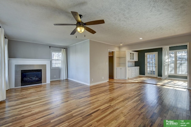 unfurnished living room with a fireplace, ornamental molding, ceiling fan, a textured ceiling, and light hardwood / wood-style flooring