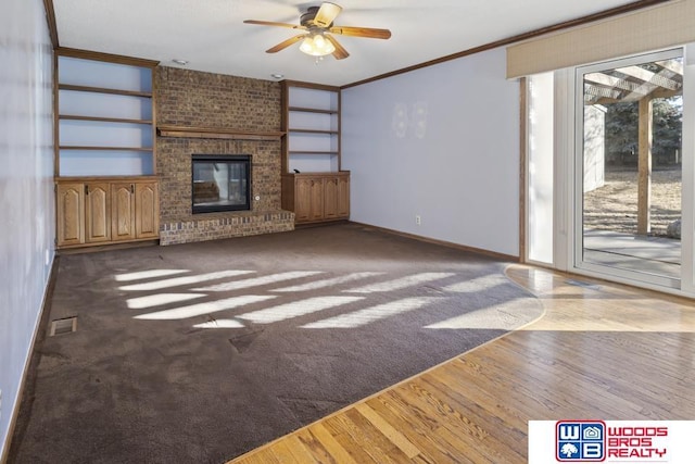 unfurnished living room featuring hardwood / wood-style floors, a fireplace, ceiling fan, crown molding, and built in shelves