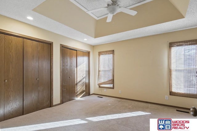 unfurnished bedroom with light carpet, two closets, and a raised ceiling