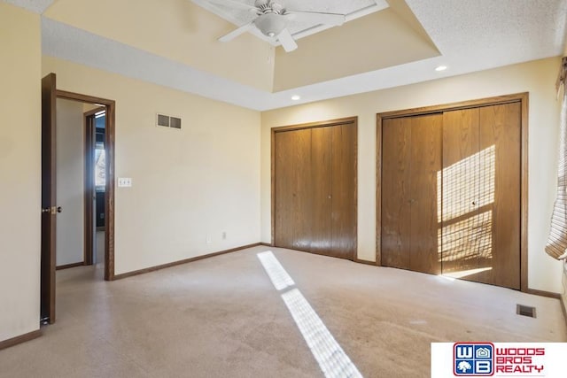 unfurnished bedroom featuring multiple closets, ceiling fan, a tray ceiling, and light carpet