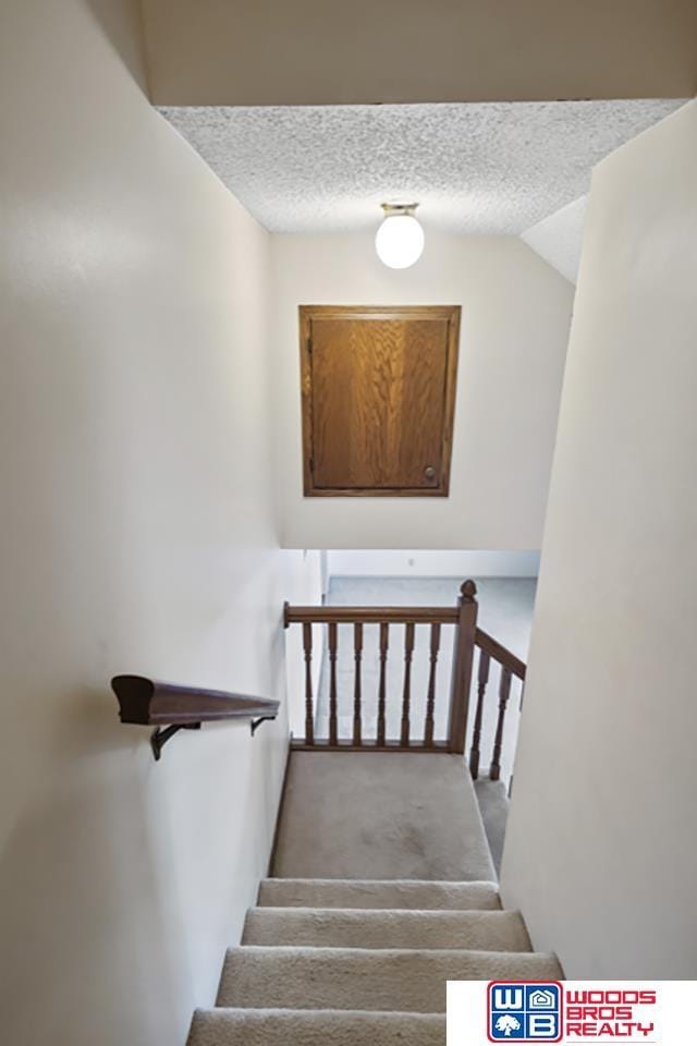 stairs with carpet floors and a textured ceiling