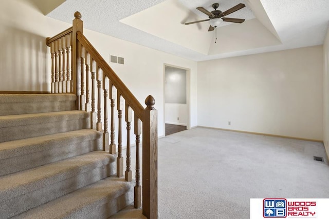 staircase with carpet flooring, ceiling fan, and a tray ceiling