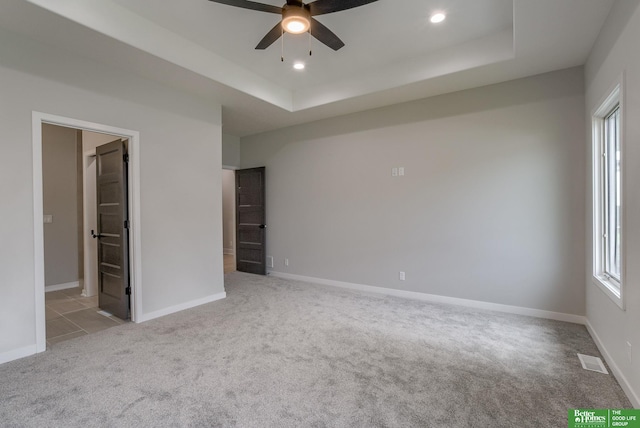 unfurnished bedroom with a raised ceiling, connected bathroom, and light carpet