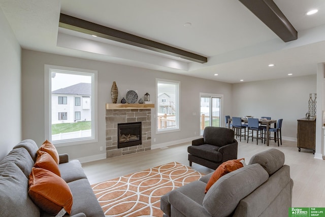 living room with beamed ceiling, a stone fireplace, and light hardwood / wood-style flooring