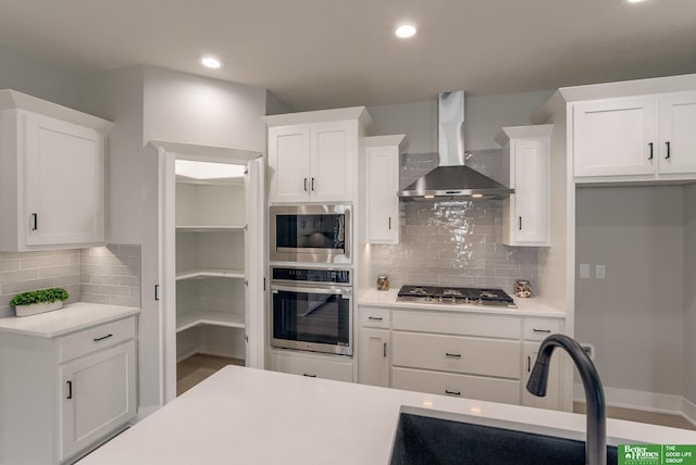 kitchen with wall chimney exhaust hood, sink, tasteful backsplash, stainless steel appliances, and white cabinets