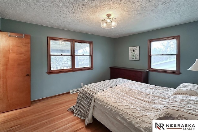 bedroom featuring light hardwood / wood-style floors, multiple windows, and a textured ceiling