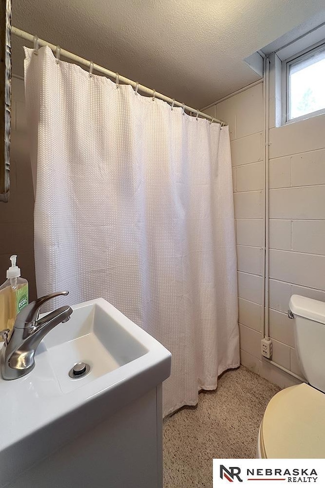 bathroom featuring a shower with shower curtain, toilet, sink, and a textured ceiling