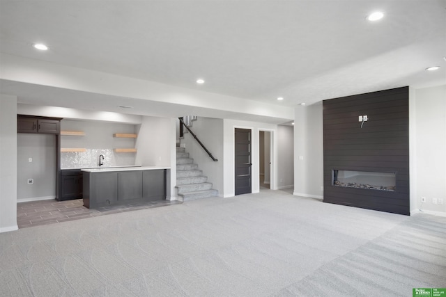 unfurnished living room featuring sink, light colored carpet, and a large fireplace