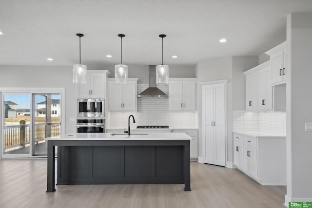 kitchen with a center island with sink, white cabinetry, sink, and wall chimney range hood