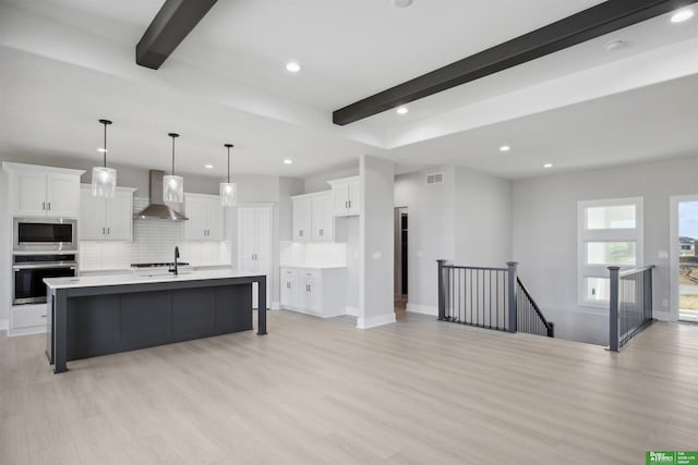 kitchen with white cabinetry, a center island with sink, wall chimney exhaust hood, and appliances with stainless steel finishes