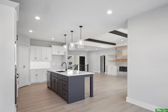 kitchen with an island with sink, white cabinets, hanging light fixtures, light hardwood / wood-style floors, and beam ceiling